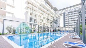 A modern apartment building with a rooftop pool area, including lounge chairs and a clear blue pool. - Bloomfields Magnificent STU in Oasis (Abu Dhabi)