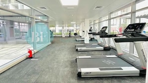 A gym with treadmills, a fire extinguisher, and large windows. - Bloomfields Magnificent STU in Oasis (Abu Dhabi)
