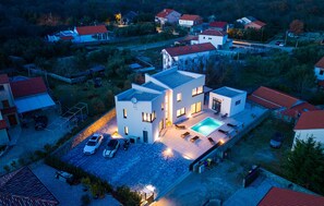 Une maison moderne avec une piscine, plusieurs voitures et une allée bien éclairée.