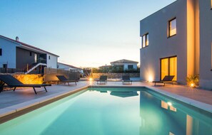 Une piscine avec des chaises longues, un mur en pierre et des bâtiments modernes en arrière-plan.