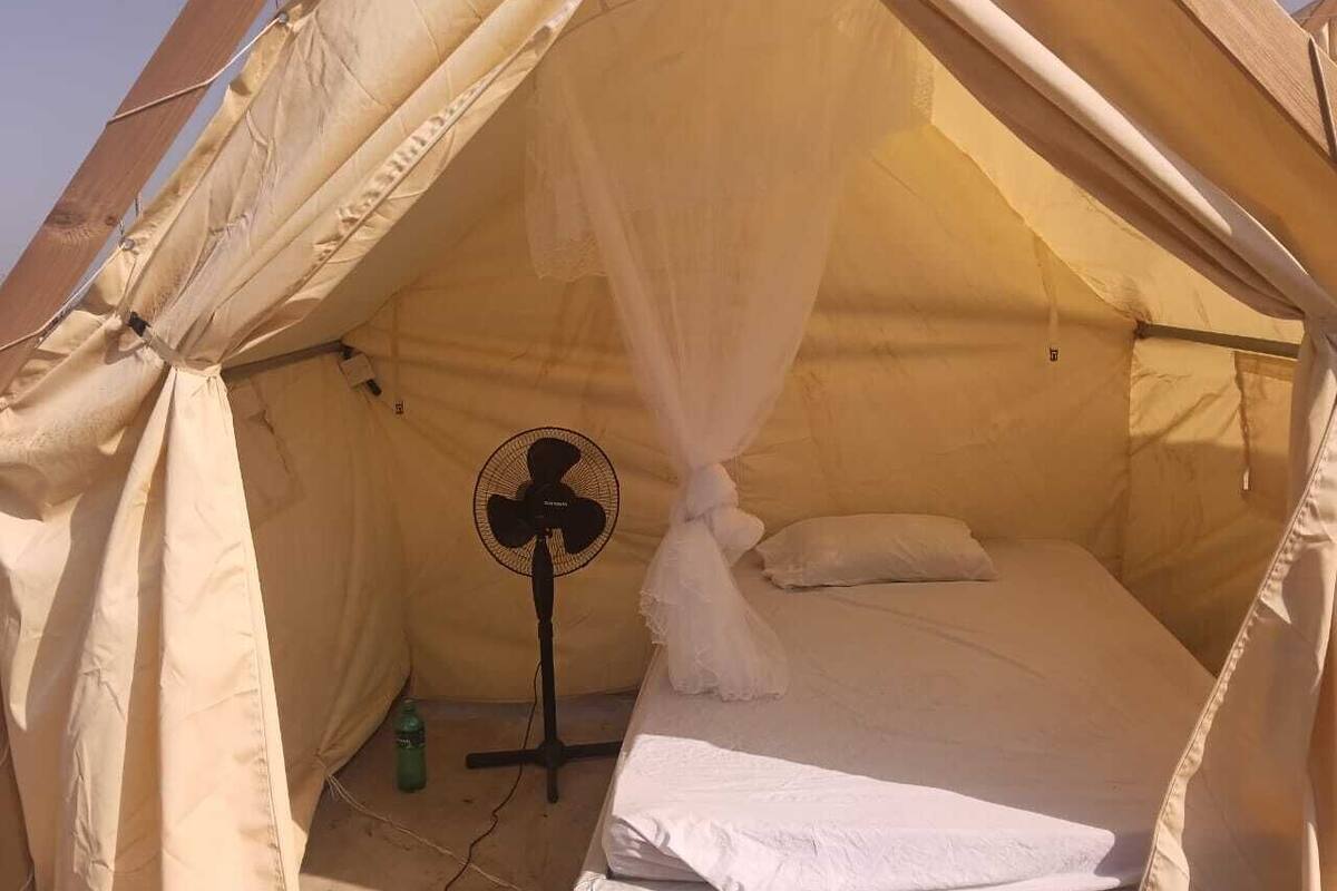 Una carpa con una cama, un ventilador y una botella.