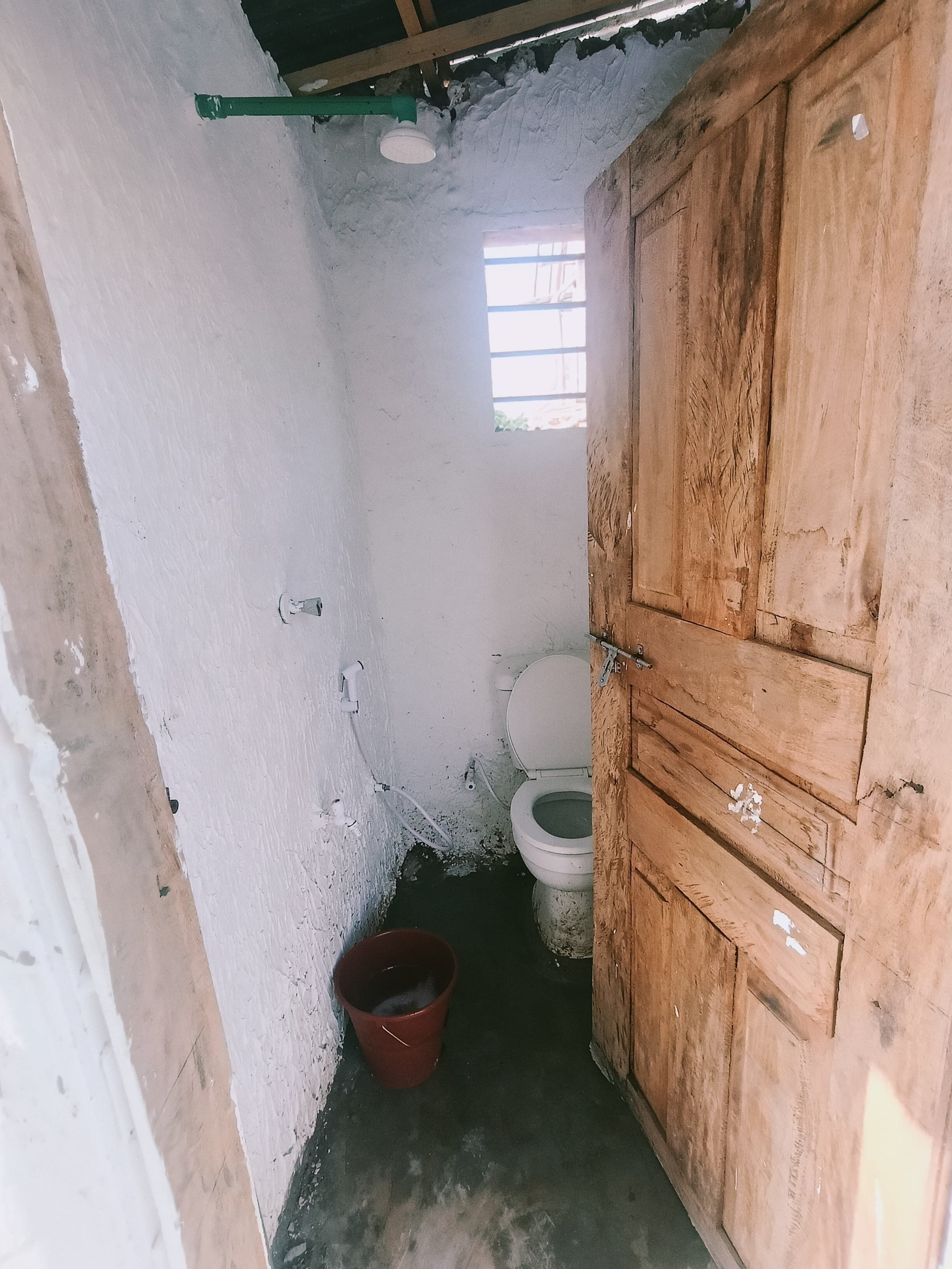 Un baño pequeño y estrecho con un armario de madera, un inodoro y un balde.