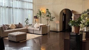 Un salon moderne avec un canapé d’angle, un petit pouf et des plantes en pot.