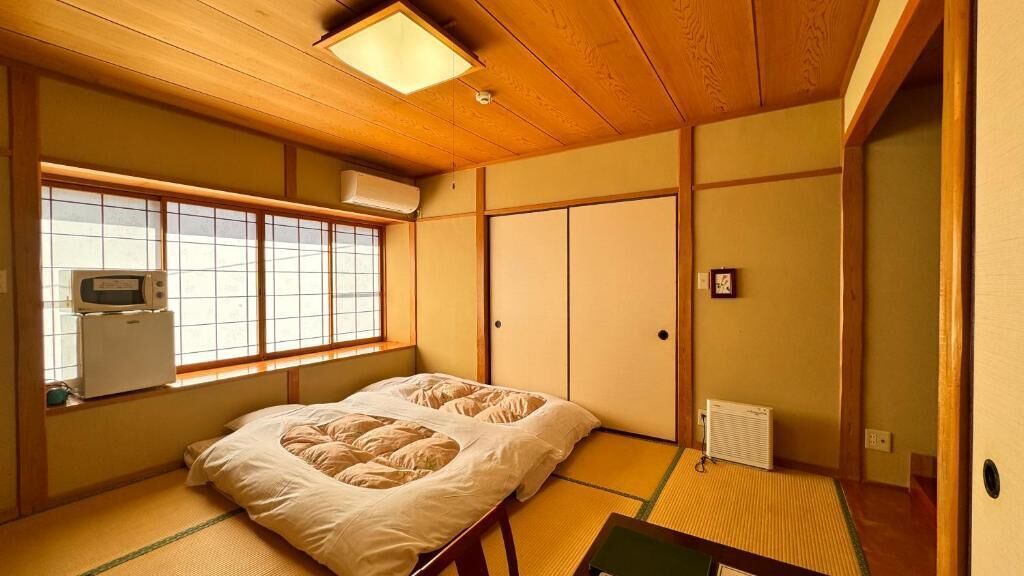 Una habitación japonesa tradicional con suelo de tatami, futón, puertas correderas y un televisor sobre una estantería baja.