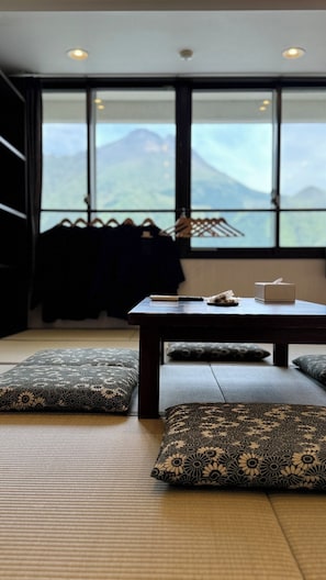 Una habitación con esteras de tatami, una mesa con una caja de pañuelos y vistas a montañas a través de amplios ventanales.