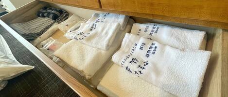 Un cajón con toallas blancas dobladas ordenadamente, algunas con texto impreso, y un par de zapatillas.