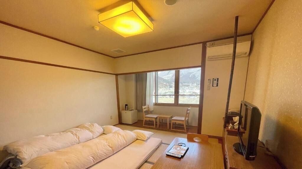A hotel room with a bed, a desk, a chair, a TV, and a window with a view of mountains.