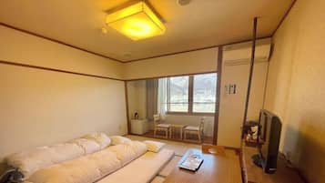 A hotel room with a bed, a desk, a chair, a TV, and a window with a view of mountains.