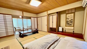 Une pièce de style japonais traditionnel, avec un sol recouvert de tatamis, une table basse, un lit, des portes coulissantes et un tableau accroché au mur.