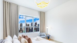 Ein modernes Hotelzimmer mit einem großen Fenster und Blick auf die Stadt, einem Bett mit ordentlich drapierten Kissen, einem Nachttisch mit Lampe sowie einem Sessel.