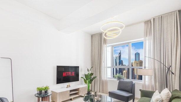 Ein modernes Wohnzimmer mit Flachbildfernseher, einer Couch, einem Couchtisch und einem großen Fenster mit Blick auf die Stadt.