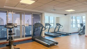 Ein Fitnessraum mit Laufbändern, Crosstrainern und Fahrrädern, große Fenster mit Blick auf die Stadt.