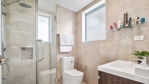 Et moderne badeværelse med brusekabine i glas, toilet i hvidt, vaskeskab med vask og et vindue.