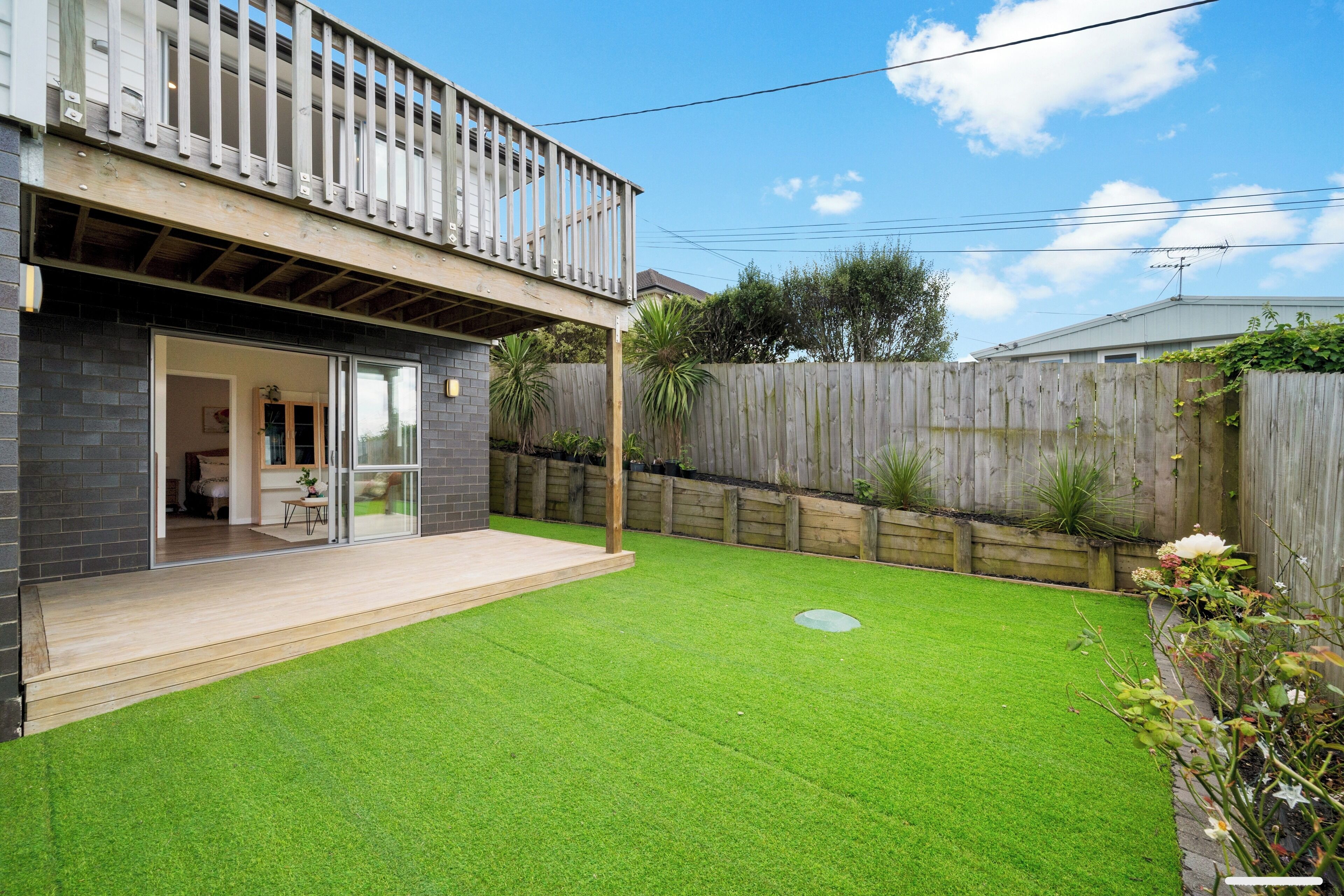 Une maison moderne dotée d’une terrasse en bois, d’un jardin clôturé et offrant une vue sur un ciel dégagé.