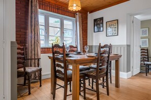 A dining area with a wooden table and chairs, a brick wall, and a window with curtains.