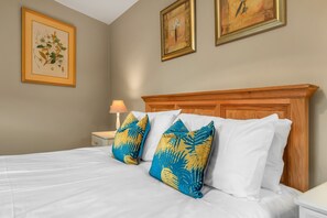 A hotel room with a wooden headboard, white bedding, and tropical-patterned pillows.