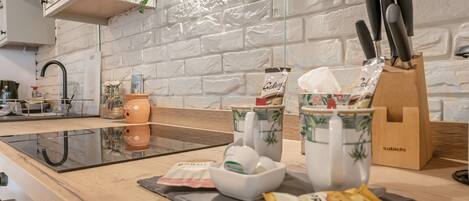 A kitchen with a white brick wall, a wooden countertop, a sink, and various kitchen items including a knife block, a bowl, and a packet of snacks.