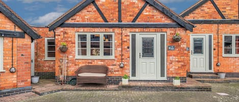 A brick building with a white door, two windows, and a bench in front.