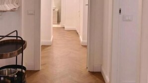 Un pasillo con piso de madera que conduce a un baño. Un carro metálico con un recipiente está a la izquierda.