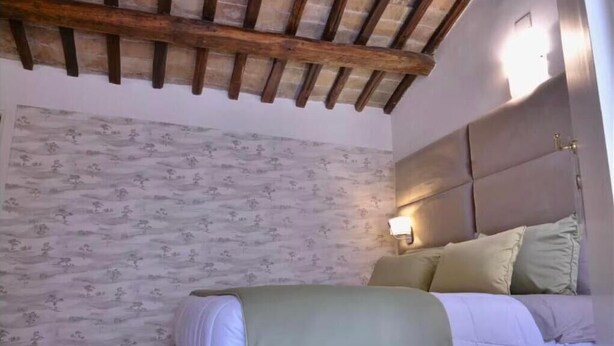 Un dormitorio con una cama, vigas de madera en el techo, un papel tapiz estampado y una mesita de noche con una lámpara.