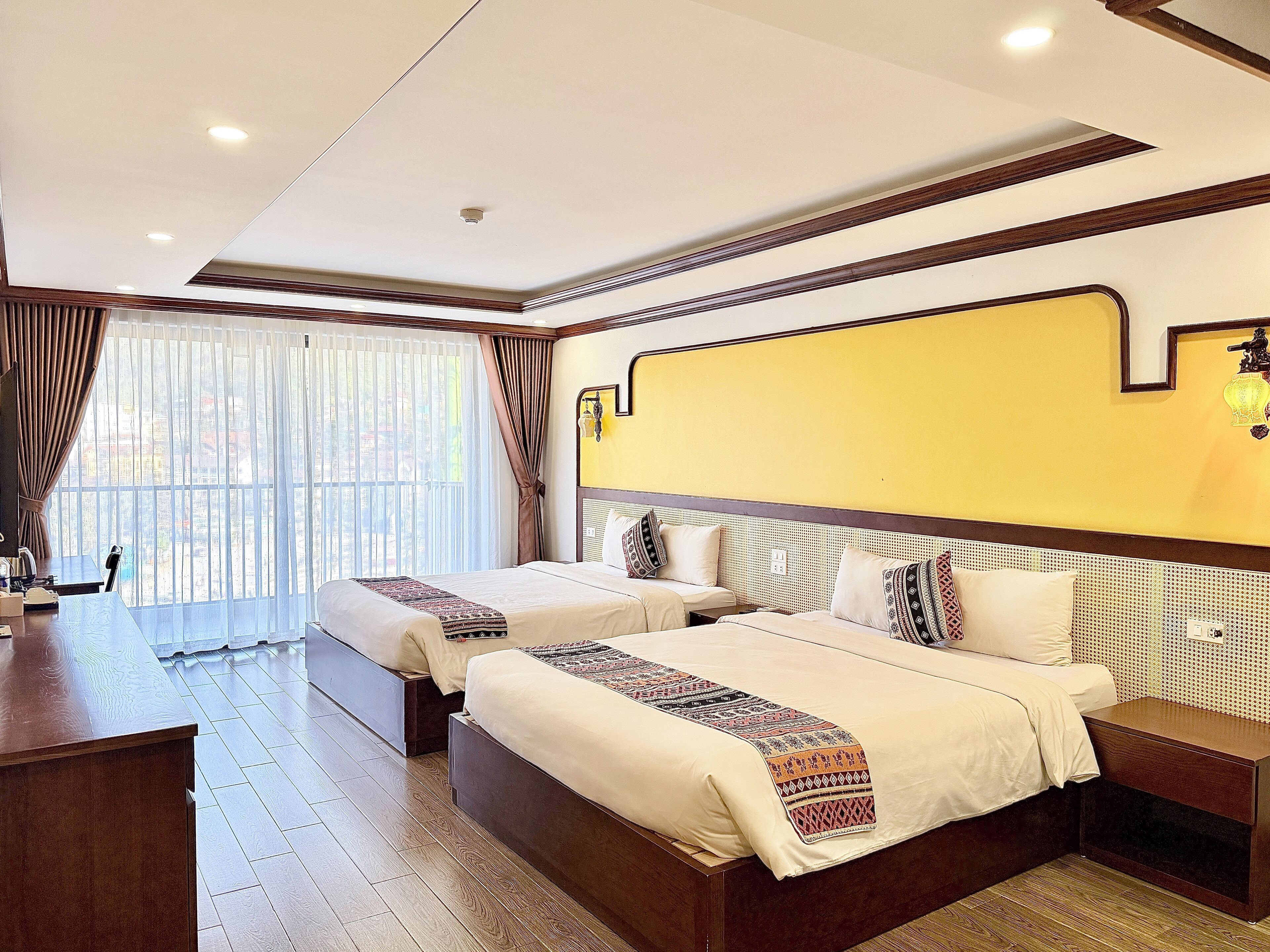 Una habitación de hotel con dos camas, un escritorio de madera y un ventanal con cortinas.