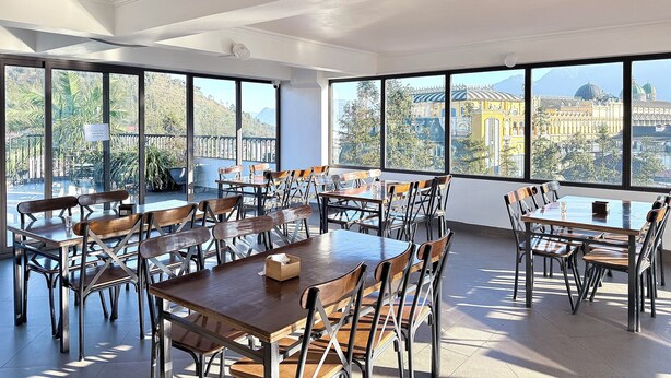 A spacious dining area with large windows offering a view of a cityscape and mountains. - Le Chapa Hotel & Spa (Sa Pa)