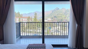 A hotel room with a large balcony, a bed, and a view of a town and mountains. - Le Chapa Hotel & Spa (Sa Pa)