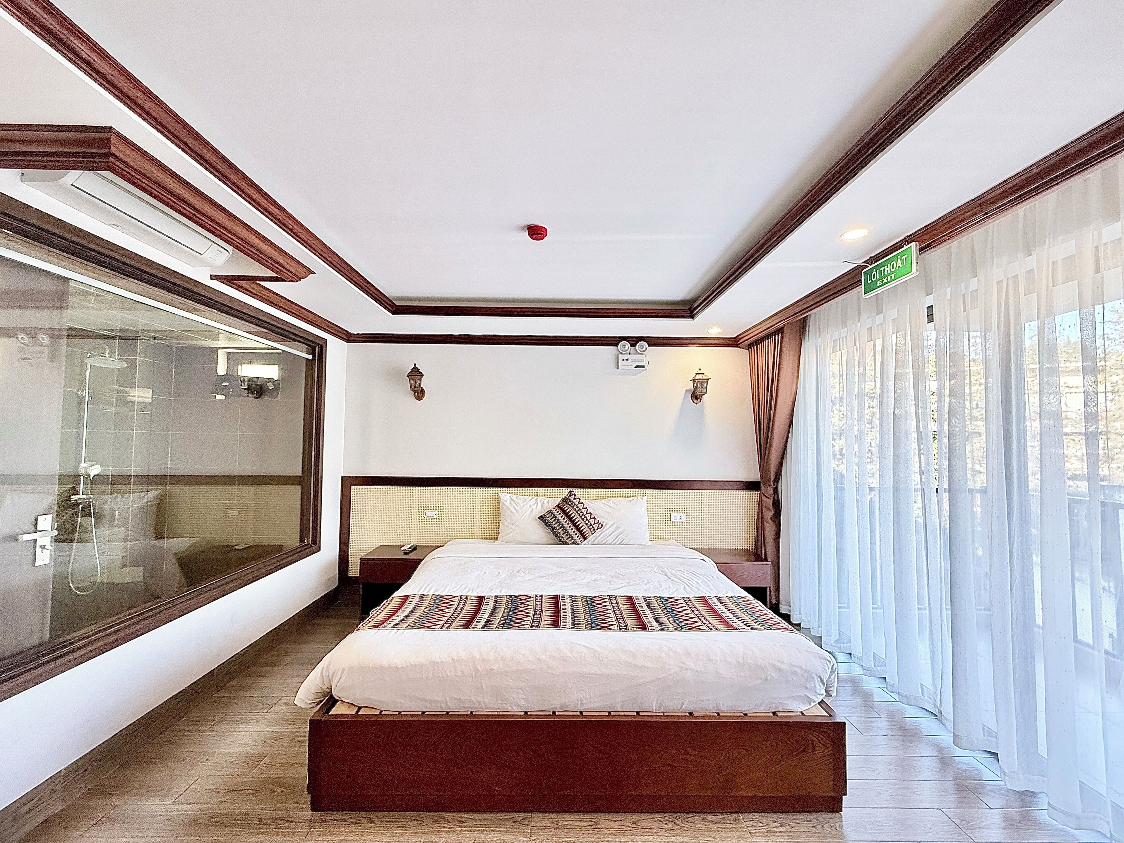 A hotel room with a large bed, a glass shower enclosure, and a view of the outdoors.