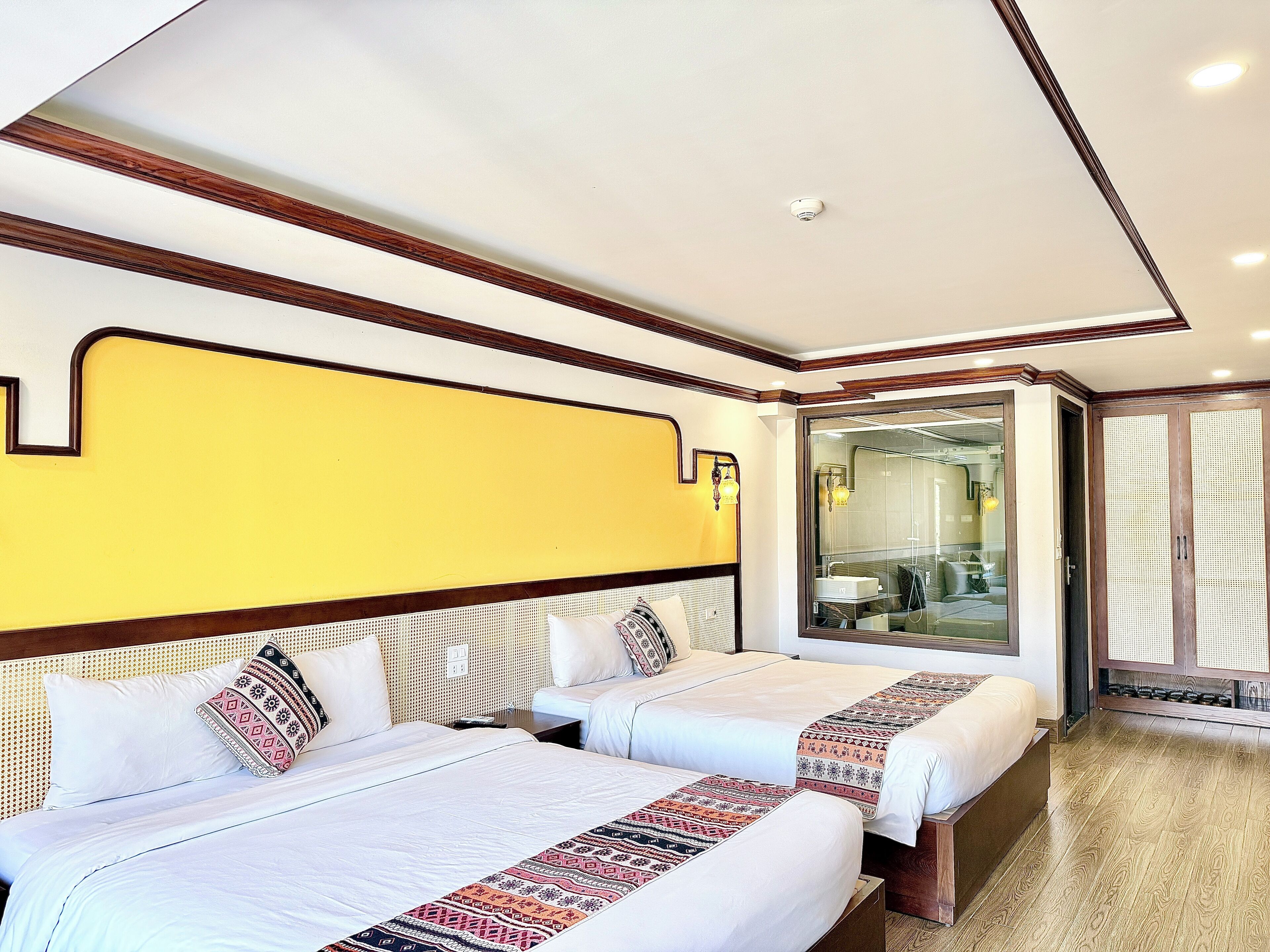 A hotel room with two beds, a mirror, and a bathroom visible through a glass door.