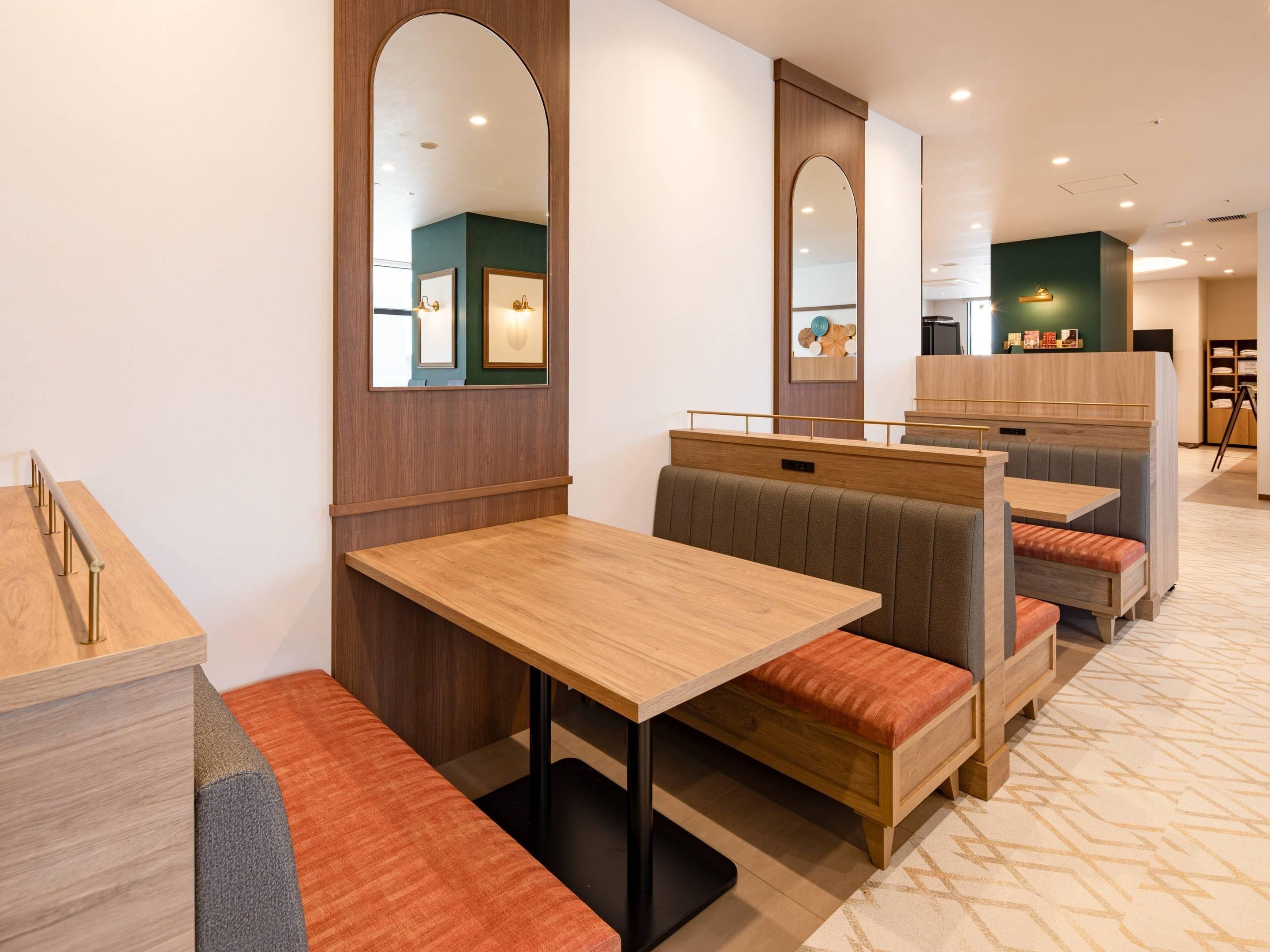 Ein modernes Restaurant mit Holztischen, gepolsterten Sitzbänken, einem gemusterten Boden und einer grünen Akzentwand.