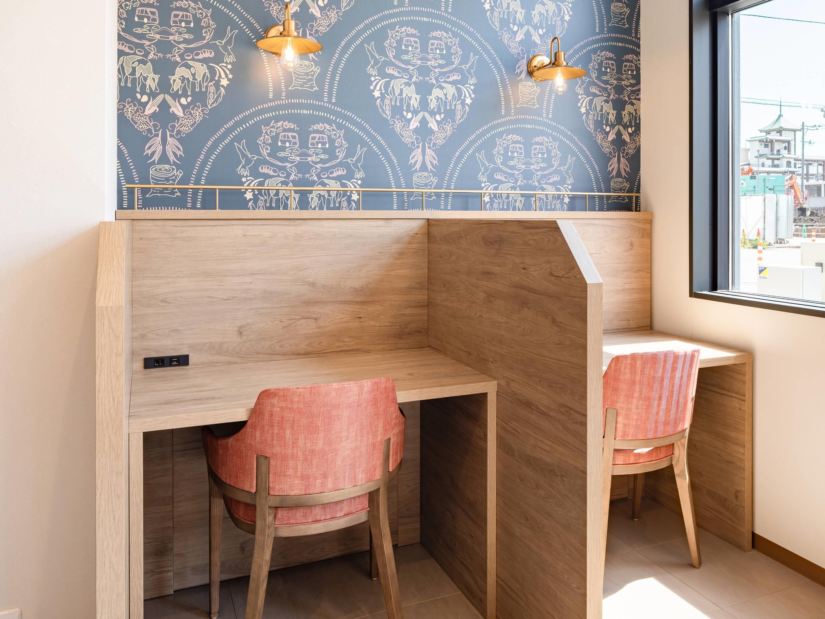 A corner workspace with two chairs, a wooden desk, and a patterned wall.