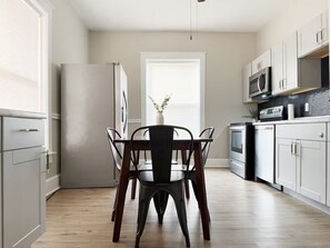 Una cucina moderna con mobili bianchi, un frigorifero in acciaio inossidabile e un'area pranzo con tavolo e sedie.