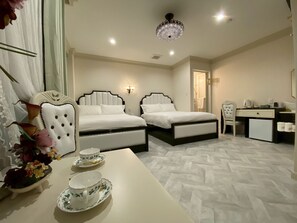 Ein Hotelzimmer mit zwei Betten, einem Schreibtisch, einem Sessel, einem kleinen Kühlschrank und einer dekorativen Kristallleuchter.