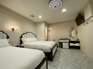 Ein Hotelzimmer mit zwei Betten, einem Schreibtisch mit Spiegel, einem kleinen Waschbecken und einem Fernseher an der Wand.