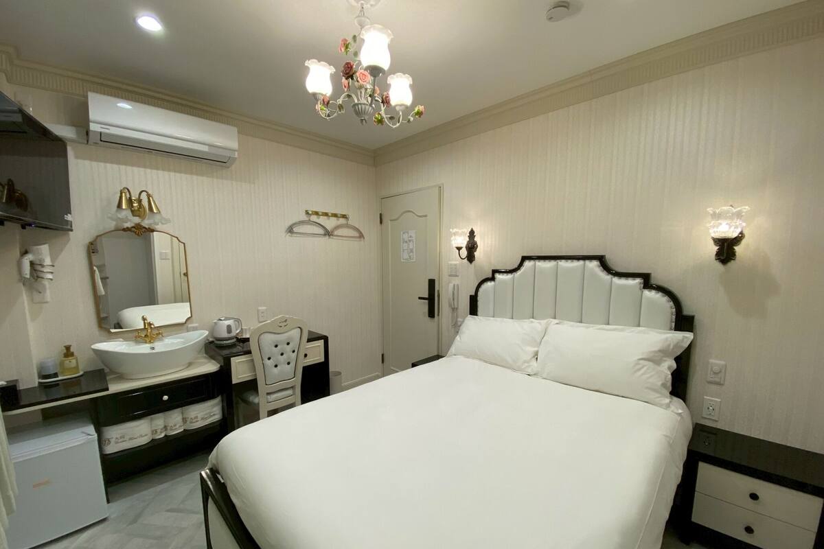 Habitación de hotel con una cama grande, una tocador con espejo, un candelabro y una lámpara de pared.