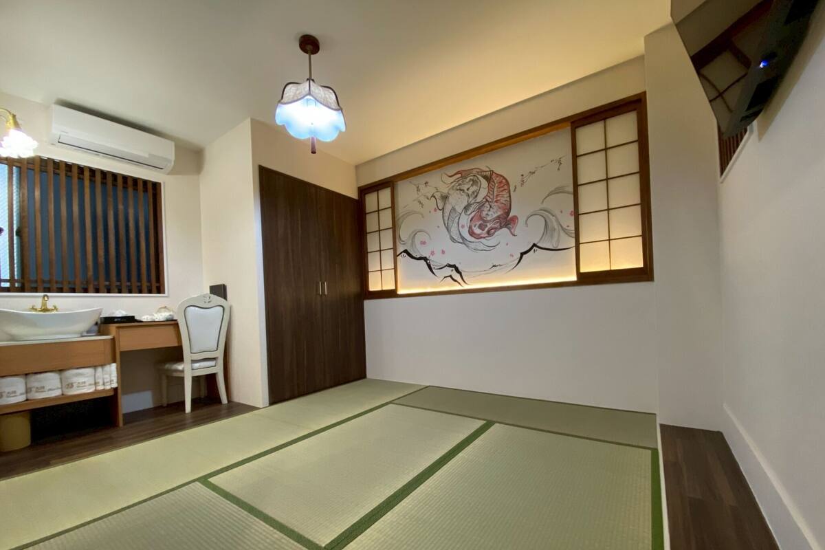 Una habitación con esteras de tatami, un armario de madera, un escritorio con una silla, aire acondicionado montado en la pared y un cuadro decorativo.