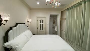 Un dormitorio ordenado con una cama grande, una araña de cristal, una puerta que da al baño y una ventana con cortinas.