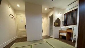 Une chambre d’hôtel avec un tatami, un plancher en bois, une salle de bain équipée d’un lavabo et d’un miroir, et une porte donnant sur une autre pièce.