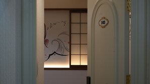 Un couloir avec une porte portant le numéro 103, une porte coulissante de style japonais traditionnel, et un mur orné d’une peinture florale.