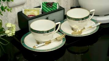 Dos tazas blancas con asas doradas y detalles turquesa, cada una con una cuchara dorada sobre un platillo a juego, sobre una superficie negra reflectante.