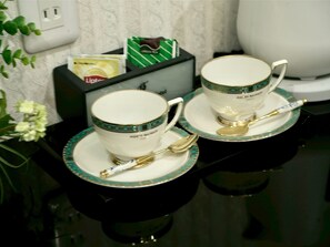 Deux tasses blanches à motifs turquoises et à anses dorées, chacune accompagnée d’une cuillère dorée posée sur une soucoupe assortie, le tout placé sur une surface noire réfléchissante.