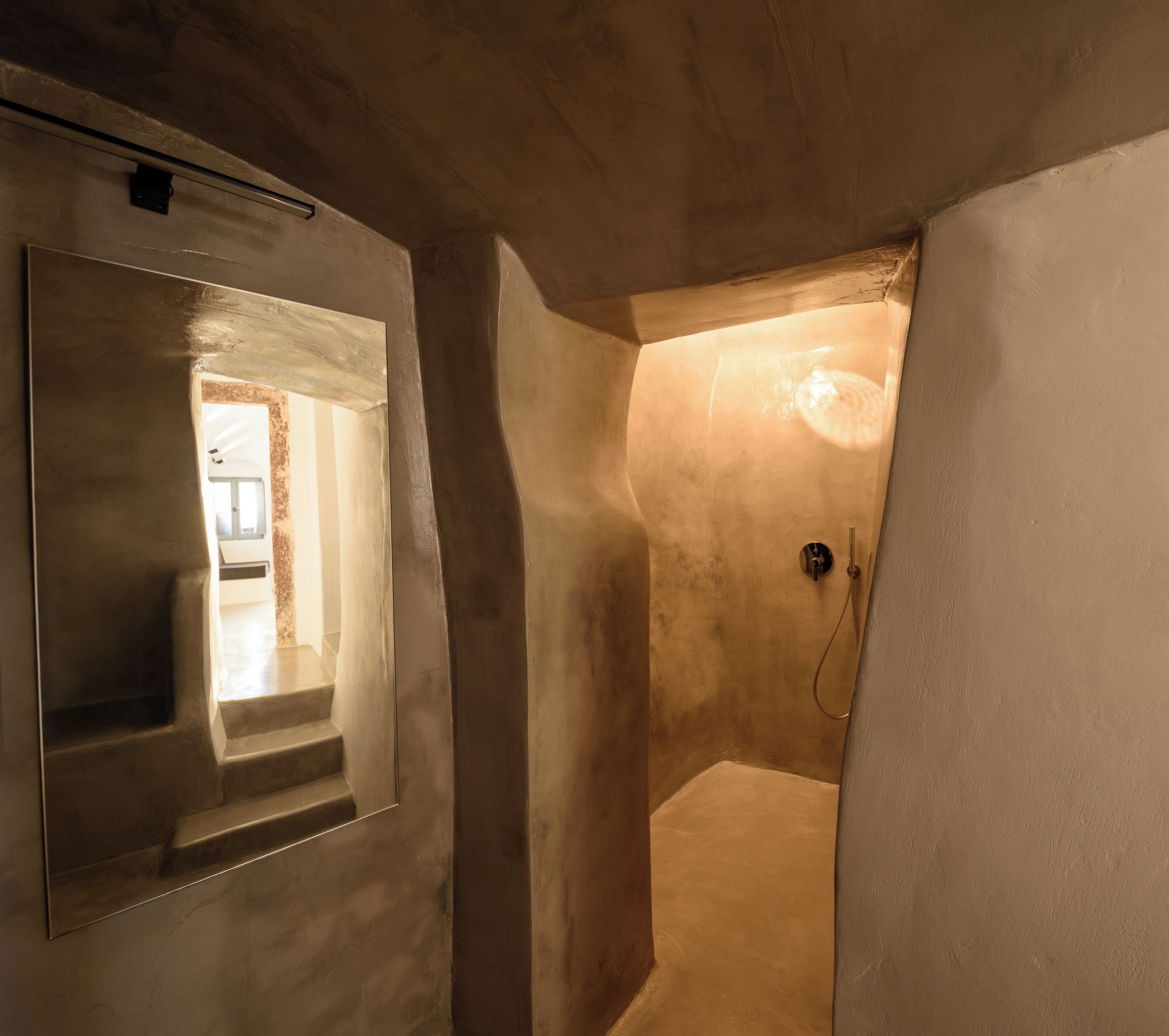 A narrow hallway with a shower area, a small window, and a door leading to another room.