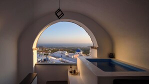 A room with a view of a town, a small pool, and a bottle of wine on a tray. - Domus Pyrgos (Santorini)