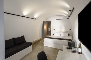 A modern hotel room with a bed, a sofa, a desk, and a TV. - Domus Pyrgos (Santorini)