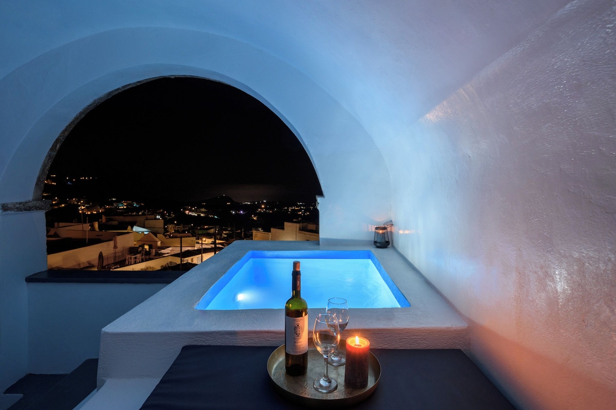 Terraza en la azotea con piscina, una botella de vino y copas sobre una bandeja, con vistas a un paisaje urbano nocturno.
