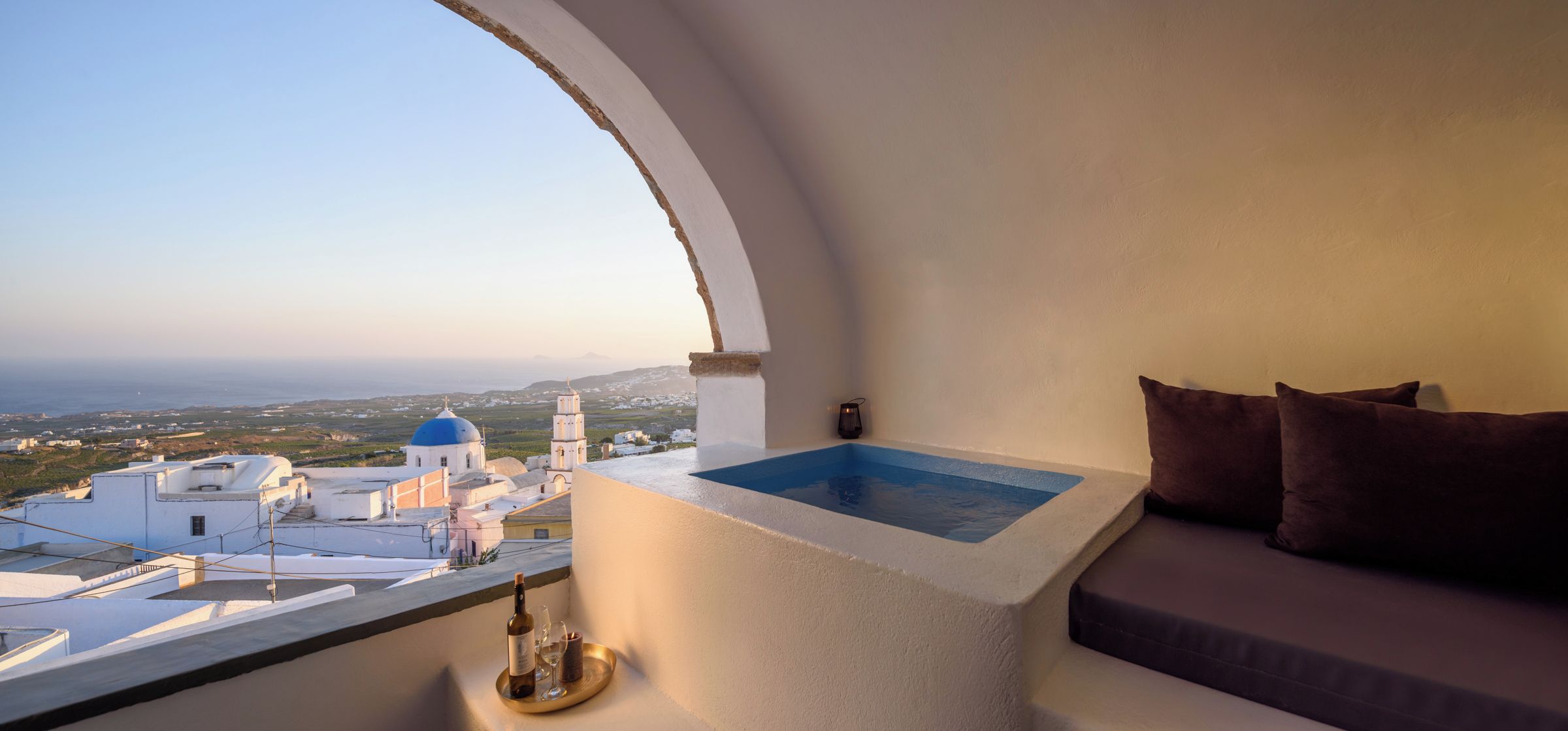 Un balcón con vistas a un pueblo costero, una piscina pequeña y un área de descanso con cojines.
