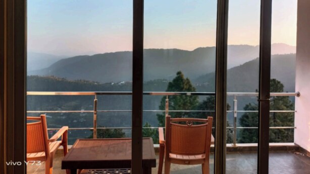 Un balcón con mesa y sillas, con vistas a montañas distantes.