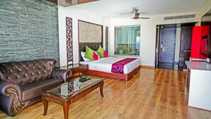Una habitación amplia con sofá de cuero, una mesa de centro de vidrio, una cama con almohadas coloridas y un ventanal grande.