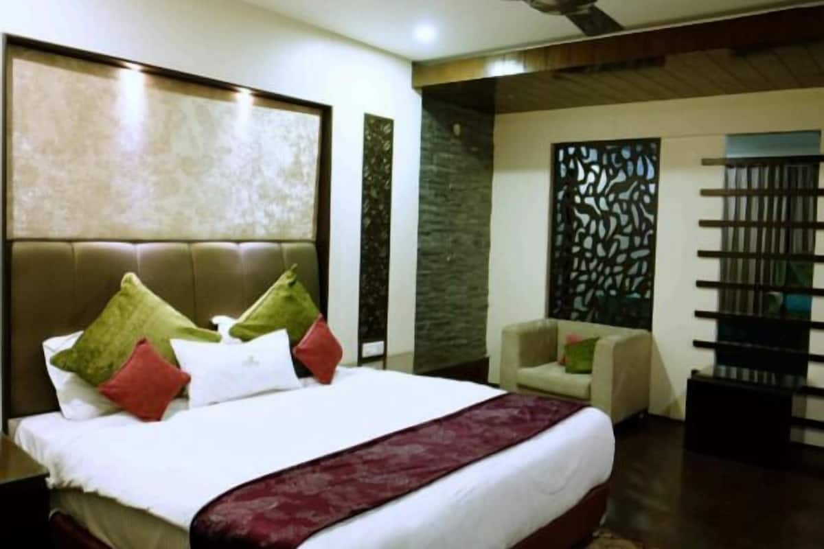 Un dormitorio con una cama grande, ventilador de techo, un panel decorativo en la pared y una pequeña zona de estar.