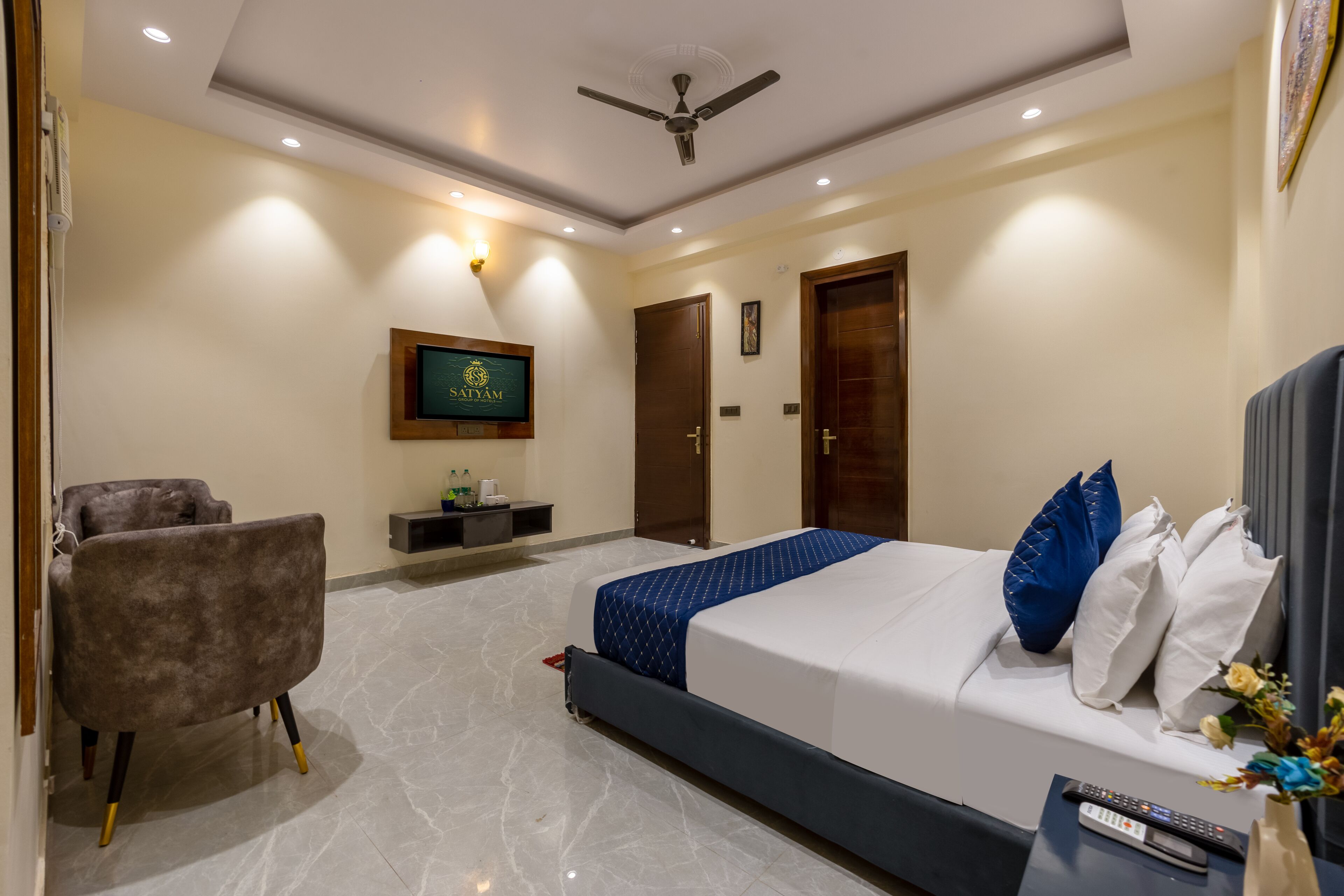 A modern hotel room with a bed, a chair, a TV, and a ceiling fan.
